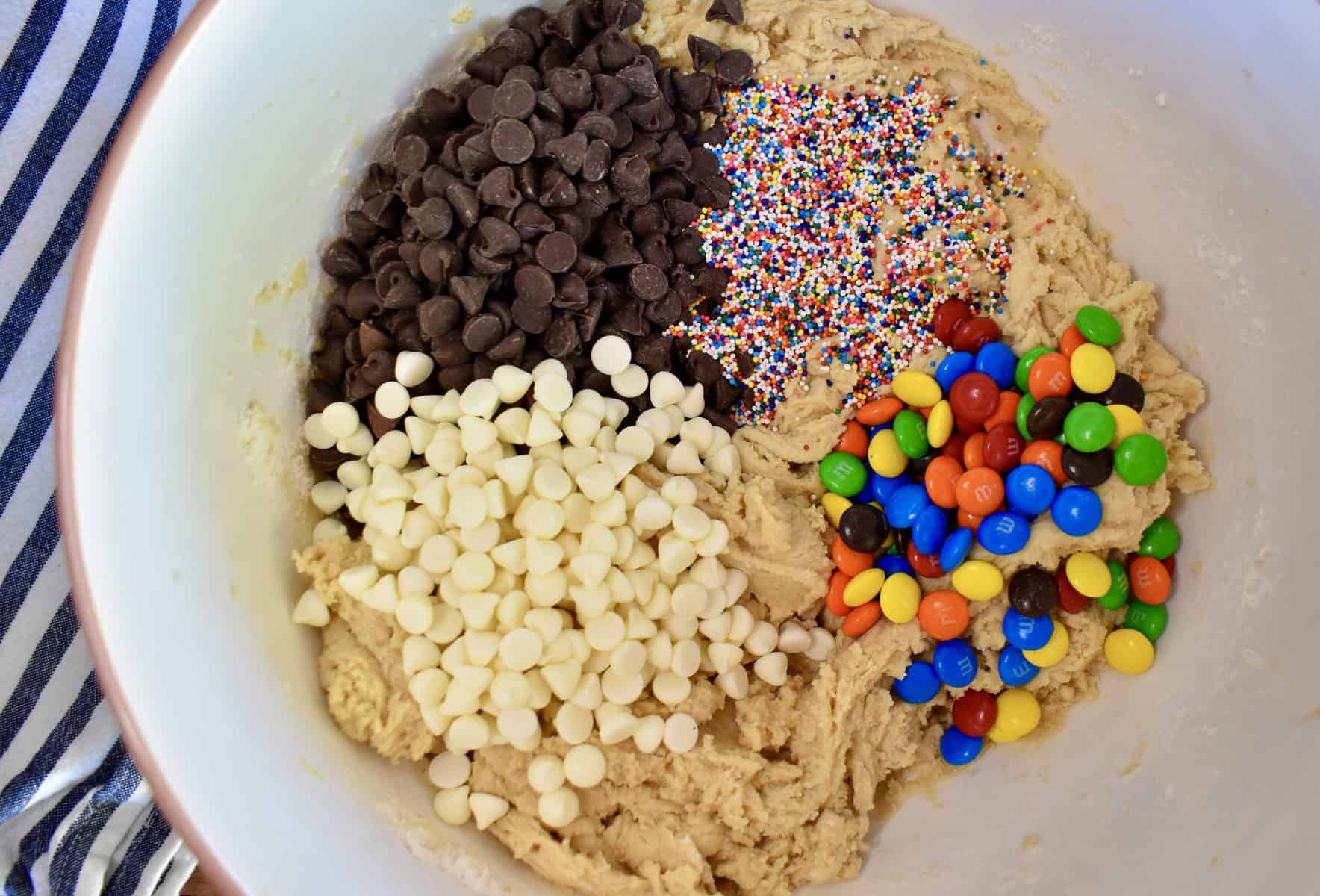 overhead photo of batter in a bowl with chocolate chip, white chips, M&M's, and sprinkles in it. 