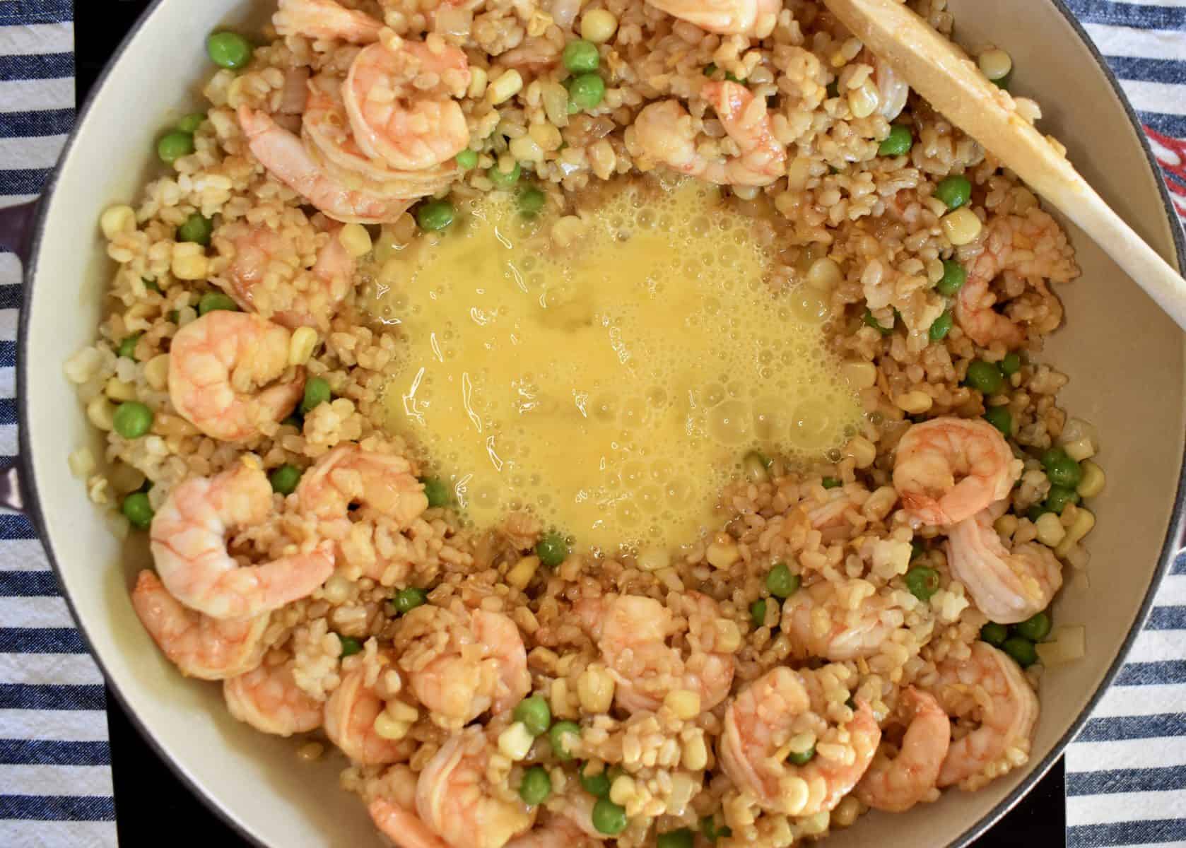 overhead photo of eggs in the middle of the pan of shrimp fried brown rice. 