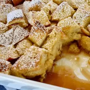 Close up of baked eggnog French toast with brown sugar glaze in a white ceramic dish.