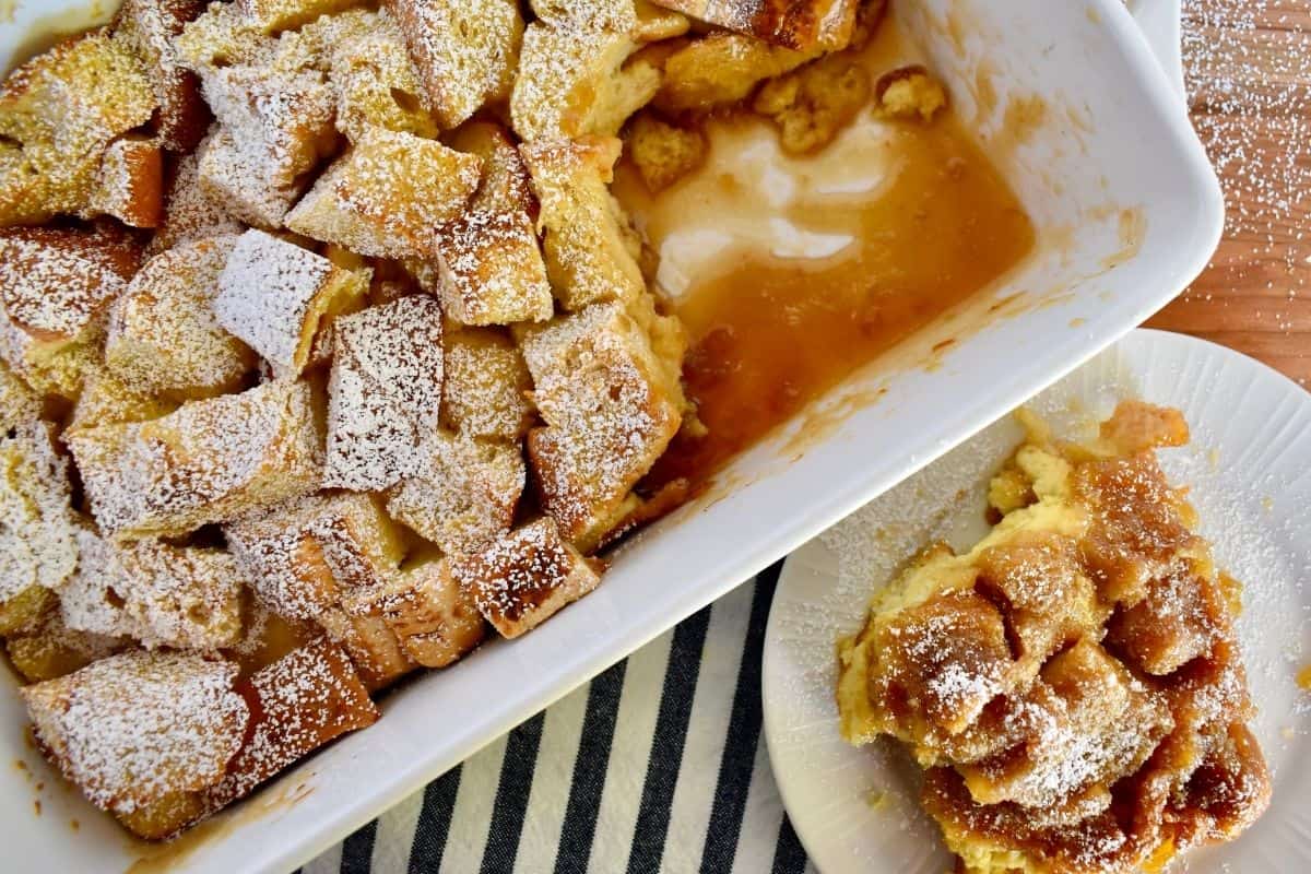 Overhead photo of eggnog French toast casserole in a white ceramic dish with a plate of the French toast next to it. 