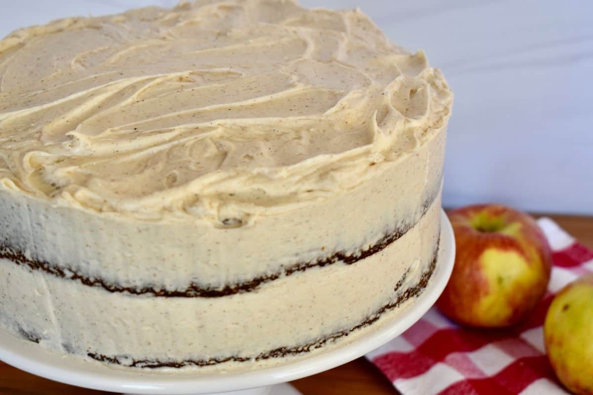 Apple Spice cake on a white pedestal with an apple in the background. 