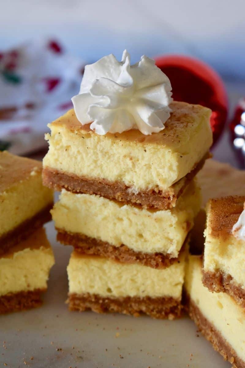 Eggnog Cheesecake bar squares stacked on each other with a dollop of whipped cream on the top one. 