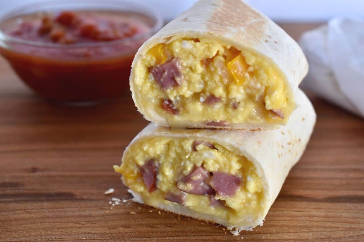 Breakfast burrito sliced in half and stacked on each other on a wooden cutting board. 