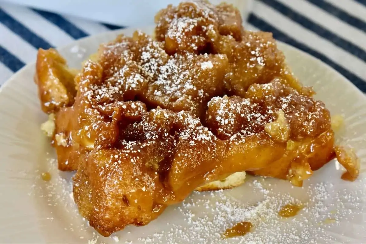 Slice of baked eggnog French toast on a white plate with a striped napkin in the background. 