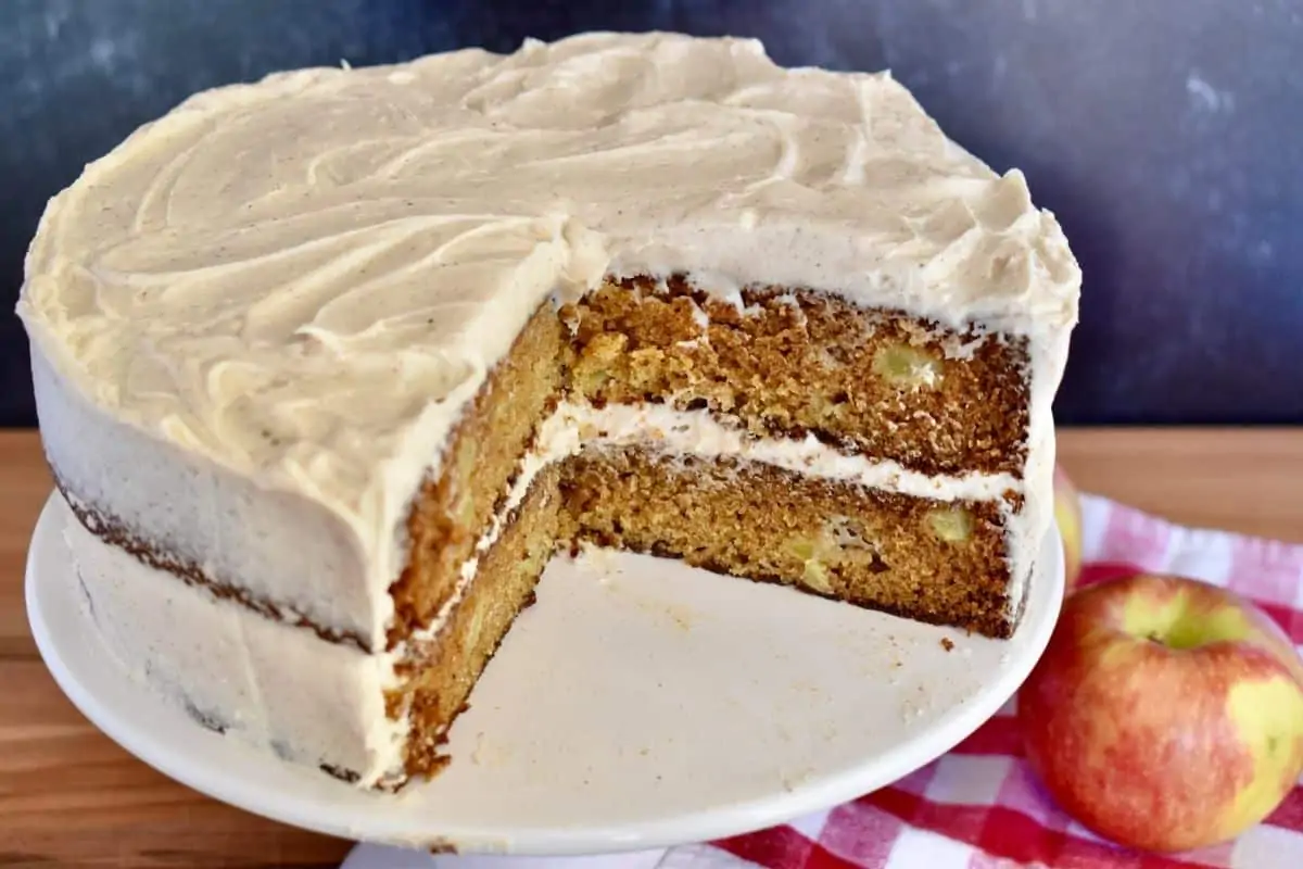 cake on a pedestal with a large slice taken out and an apple behind it. 