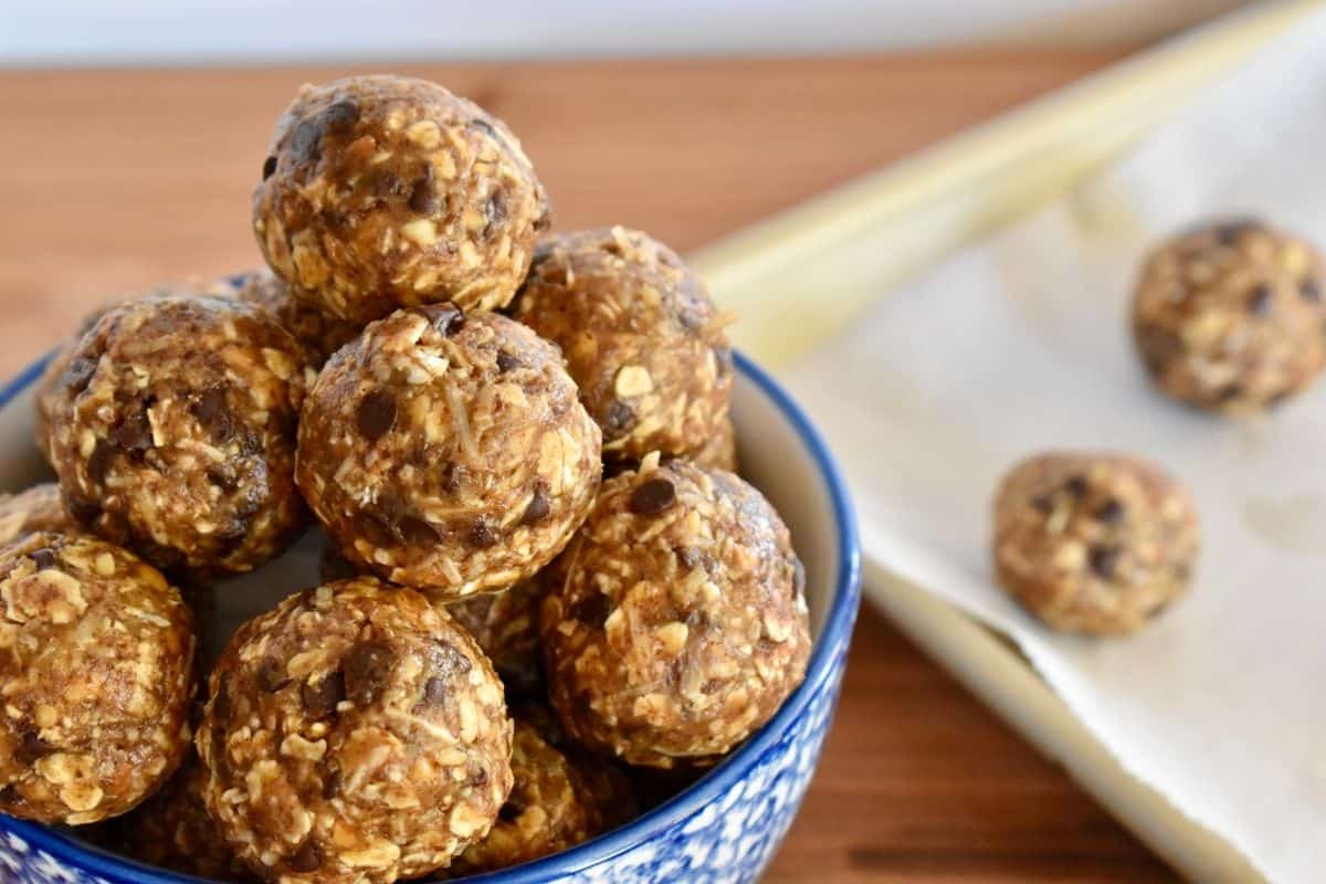 energy balls stacked high in a blue bowl with extra balls on a baking sheet in the background. 