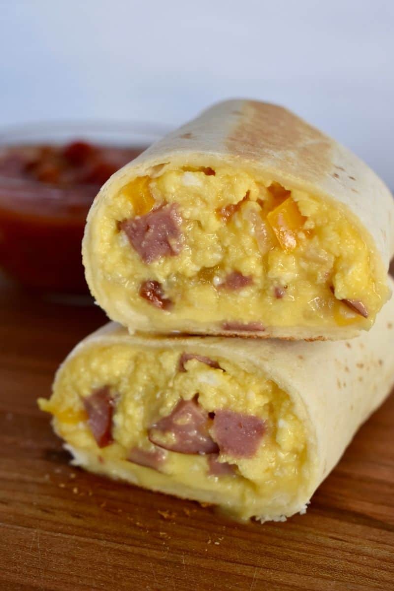 Freezer Breakfast burritos with turkey sausage stacked on each other on a wood cutting board. 