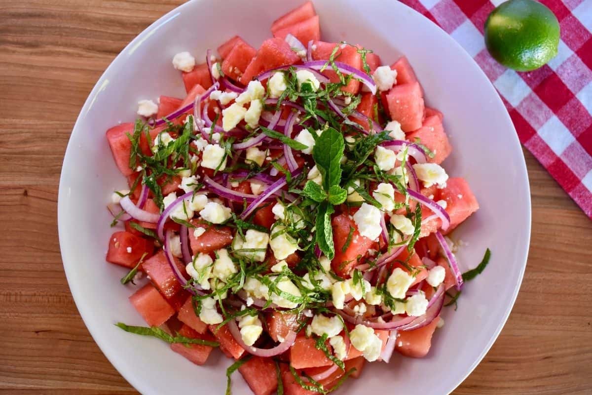 overhead photo of a white bowl filled with watermelon, feta crumbles, diced red onion, and mint. 