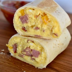 breakfast burrito cut in half and stack on each other with a bowl of salsa in the background.