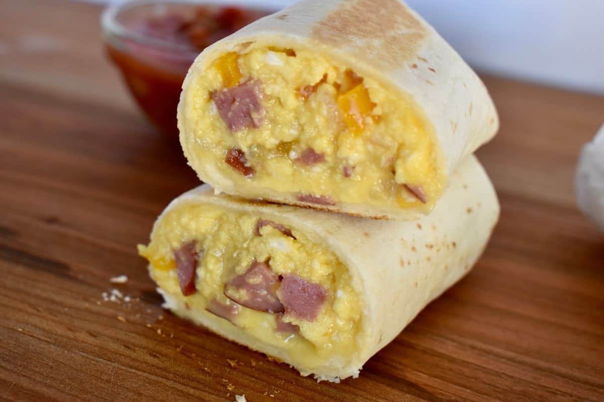 Breakfast burrito with turkey sausage cut in half and stack on each other on wood cutting board. 