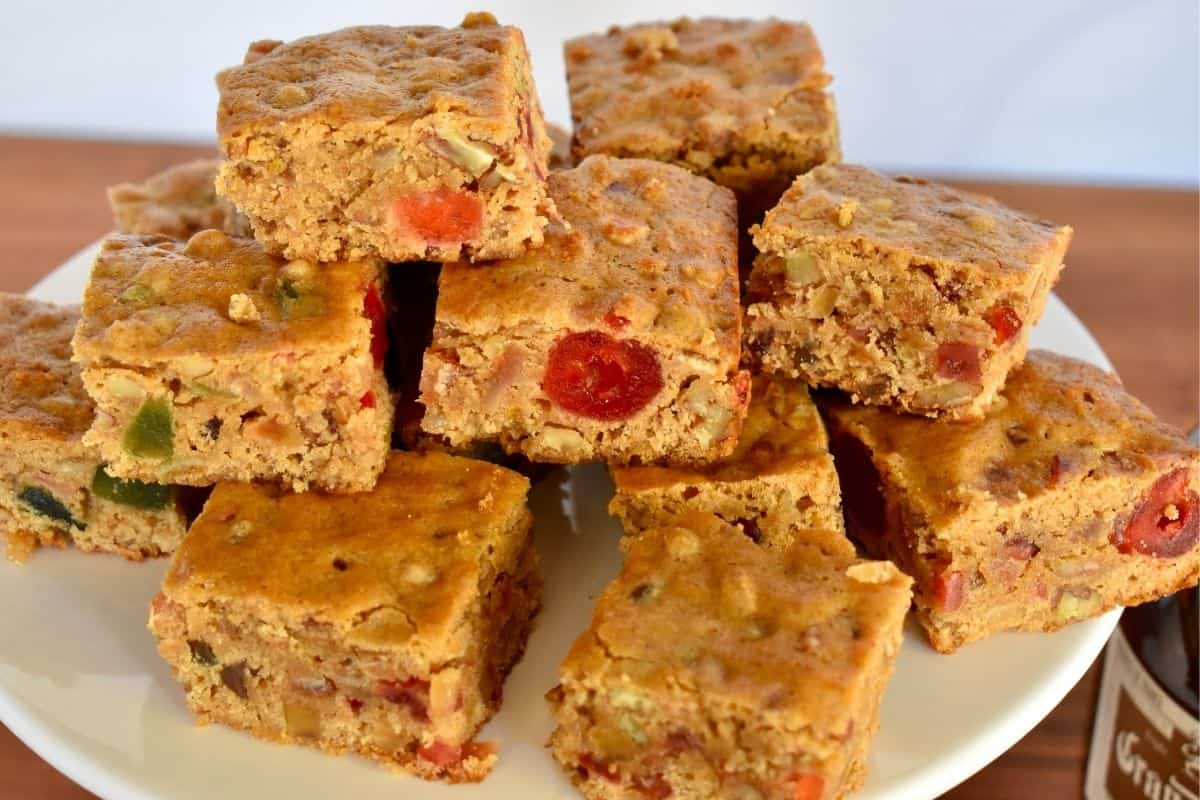 Fruitcake cookie bars piled on a white pedestal. 