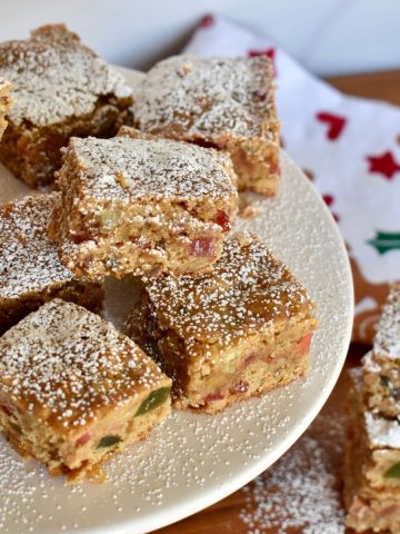 fruitcake cookie bars on a white pedestal dusted with powdered sugar.