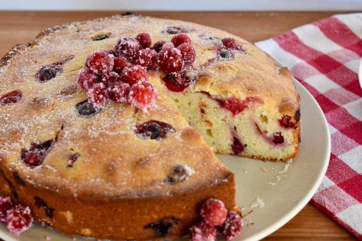 Cranberry Ricotta Cake on a white serving plate with a checkered napkin behind it. 