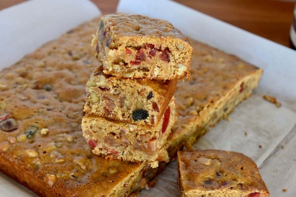 Fruitcake cookie bars sliced and stacked on each other on a piece of parchment paper. 