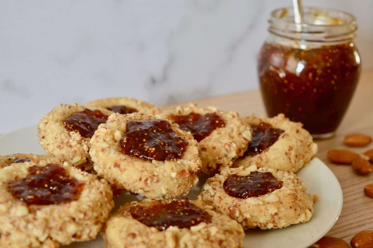 Italian Thumbprint cookies on a plate with a jar of fig jam next to it. 