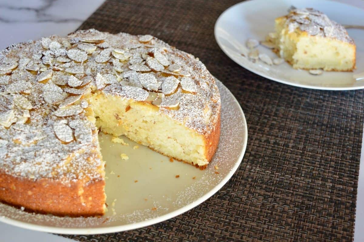 Almond ricotta cake on a white plate with a slice of it in the background. 