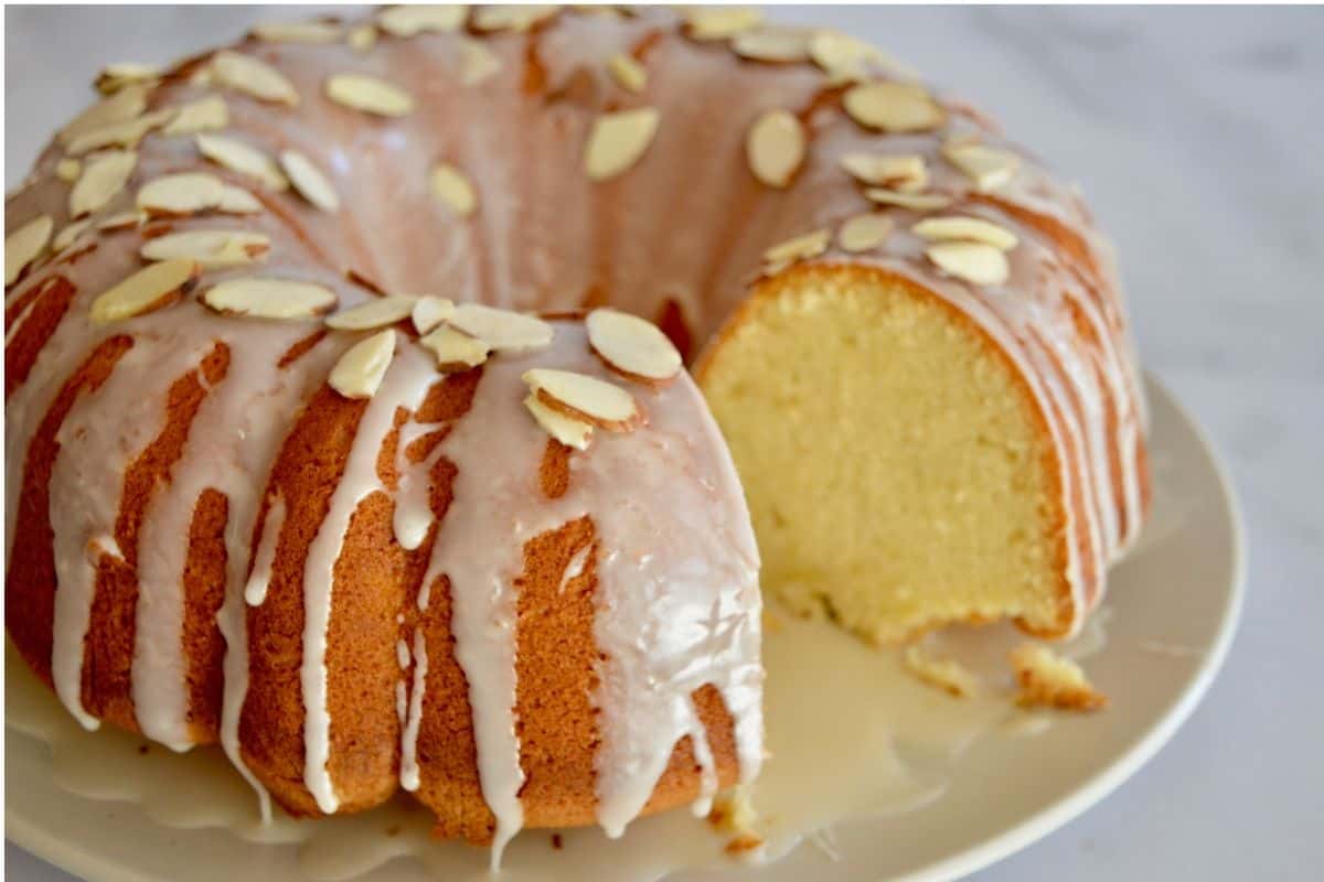 Amaretto pound cake with glaze and sliced almonds on a white platter. 
