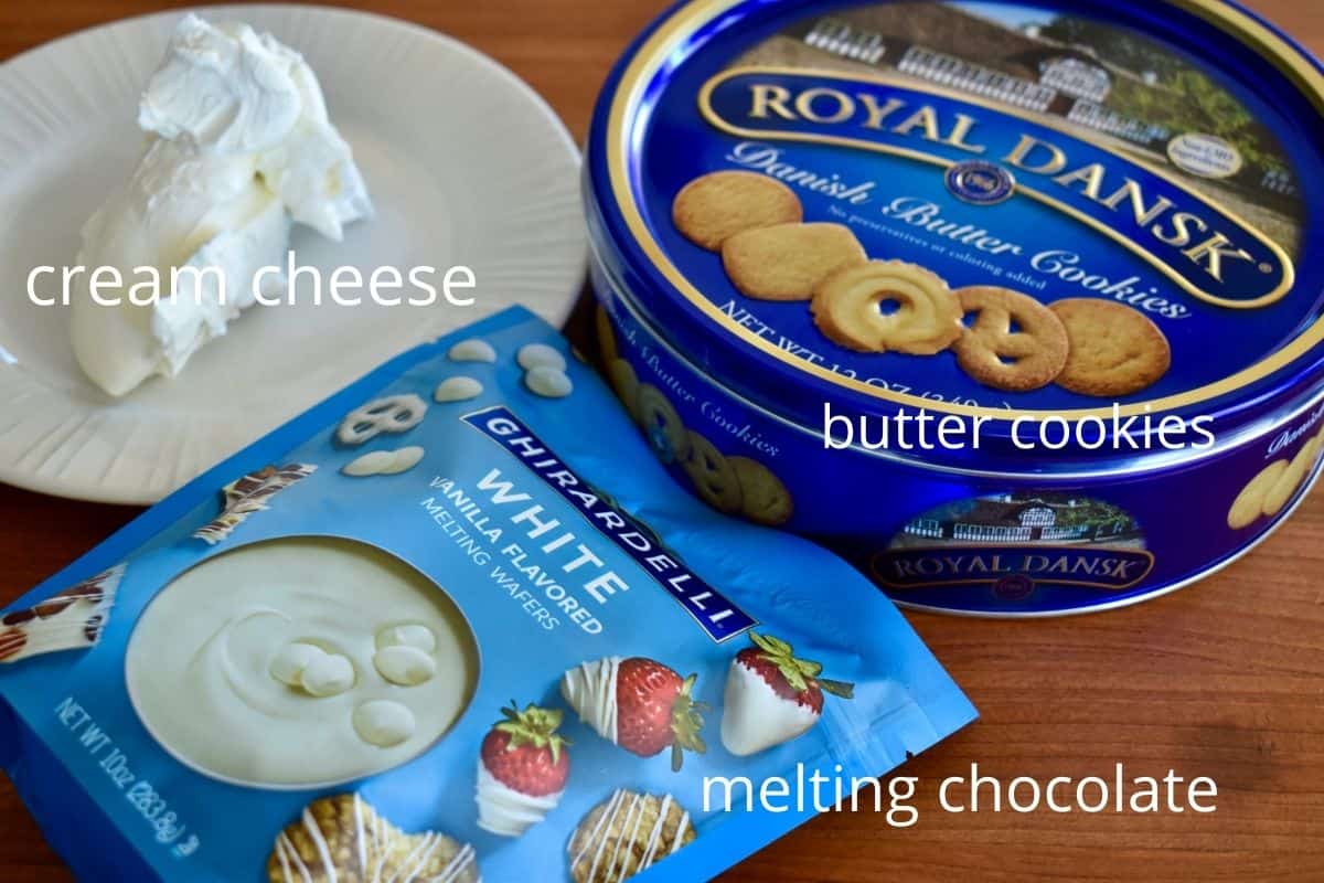 photo of ingredients needed for recipe include white melting chocolate, tin of cookies, and cream cheese. 