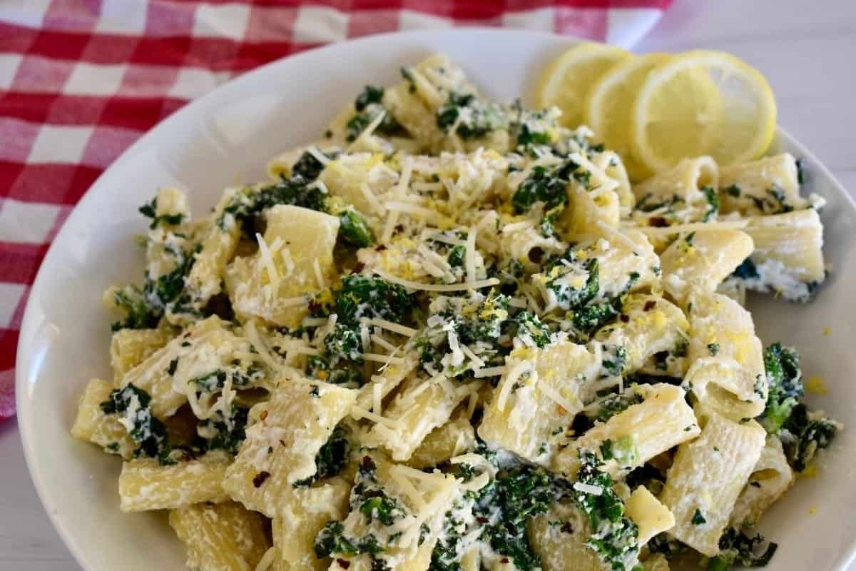 Lemon ricotta pasta recipe in a white serving plate with slices of lemon on a checkered napkin. 