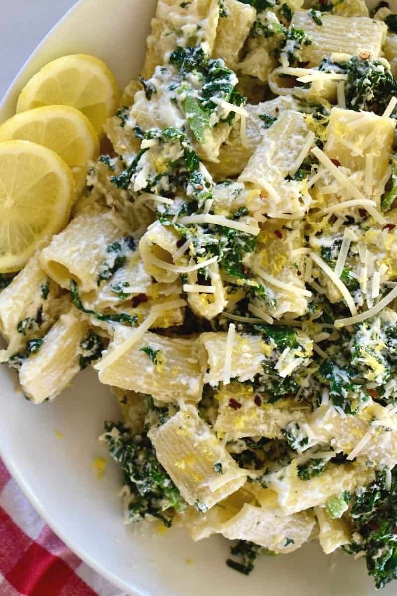 Lemon ricotta pasta with kale in a white bowl with lemon slices next to it. 