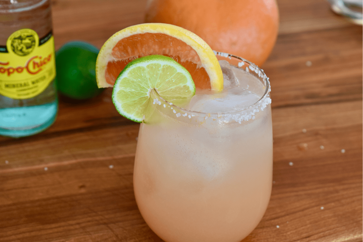 Cocktail glass with grapefruit paloma on a wood cutting board. 