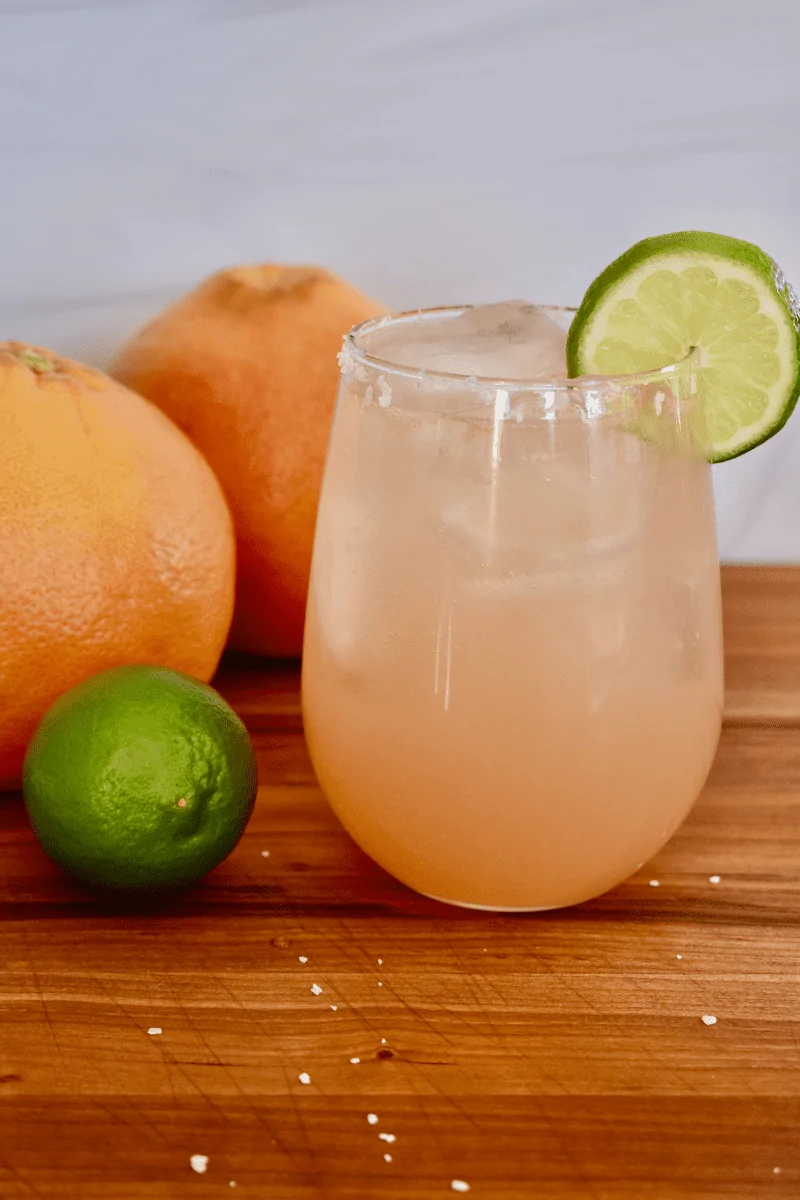 grapefruit paloma on a countertop with lime and grapefruits next to it. 