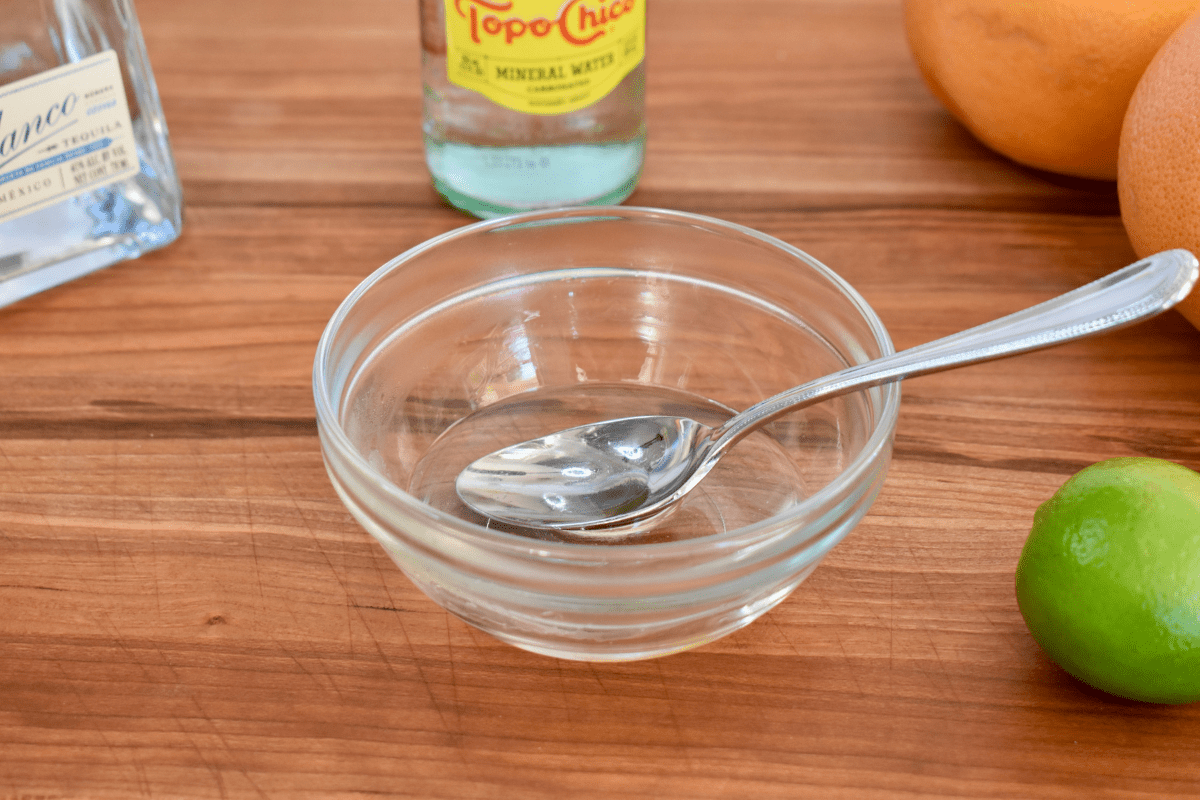 clear bowl with a simple sugar mixture in it and a spoon. 