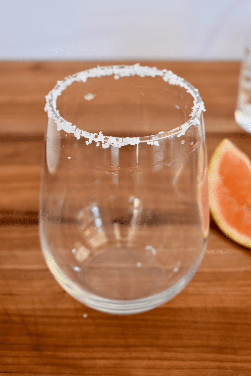 cocktail glass on a countertop with a salt rim and slice of citrus fruit next to it. 