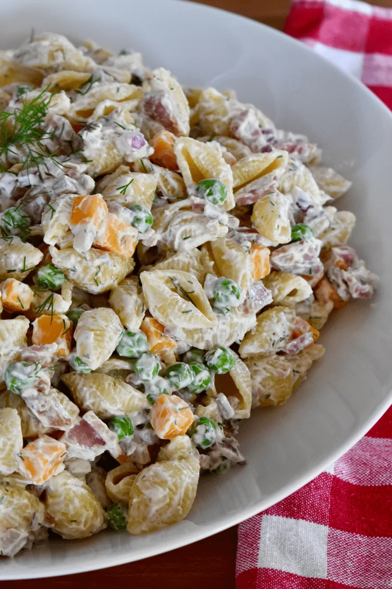 Ham pasta salad in a white bowl with a checkered napkin in the background. 