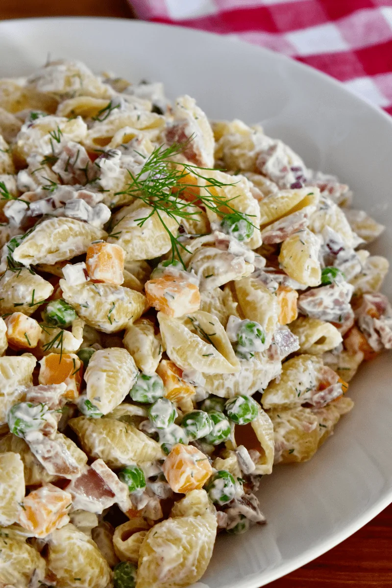 ham pasta salad in a white bowl with dill, red onions, cheddar cheese, and a greek yogurt dressing. 