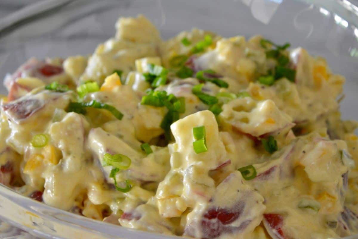 close up photo of potato salad with red potatoes in a glass serving bowl. 
