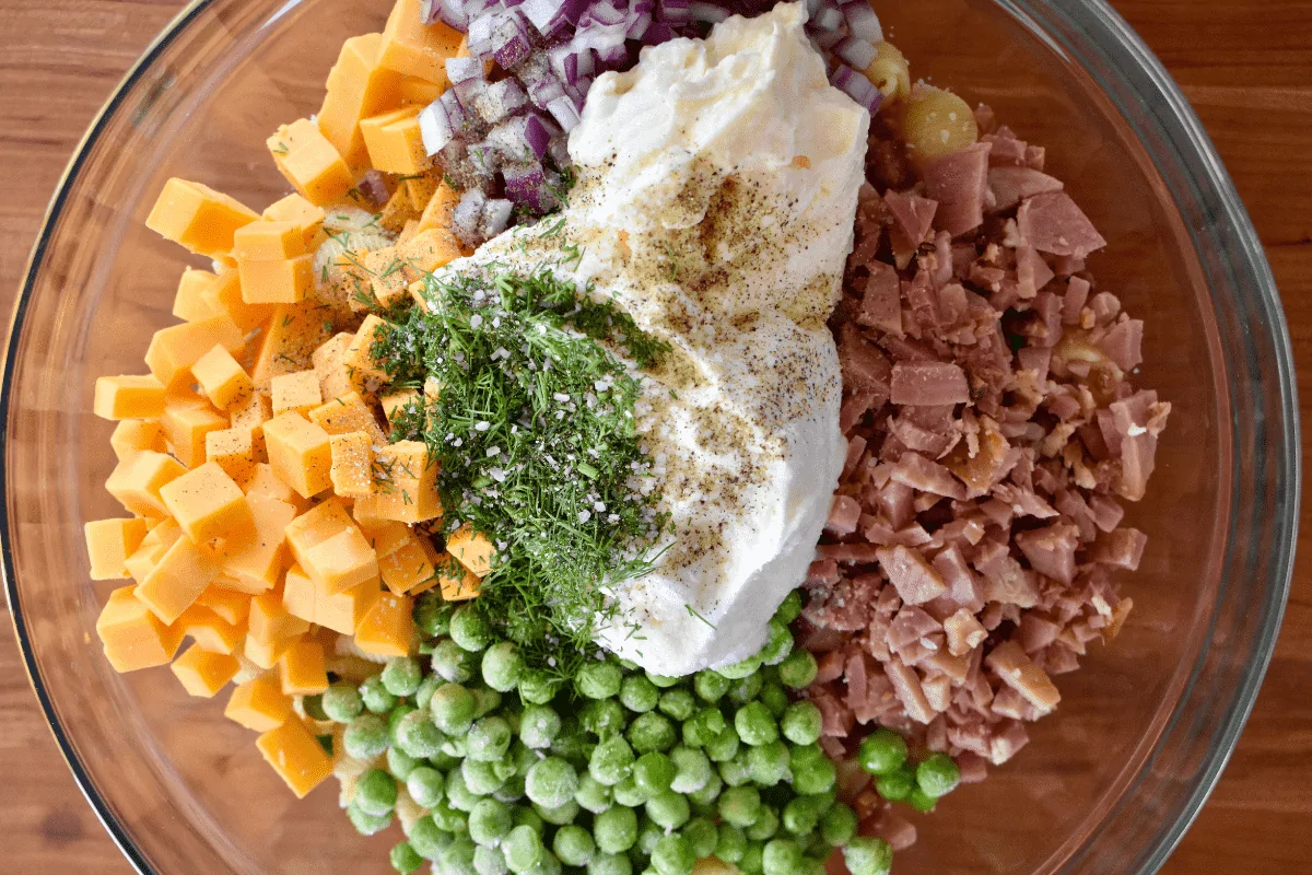 overhead photo of the ingredients in a glass mixing bowl with greek yogurt, mayo, and dill on top. 