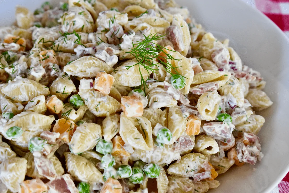 Ham Pasta Salad with dill, cheddar, peas, and red onions, in a white bowl. 