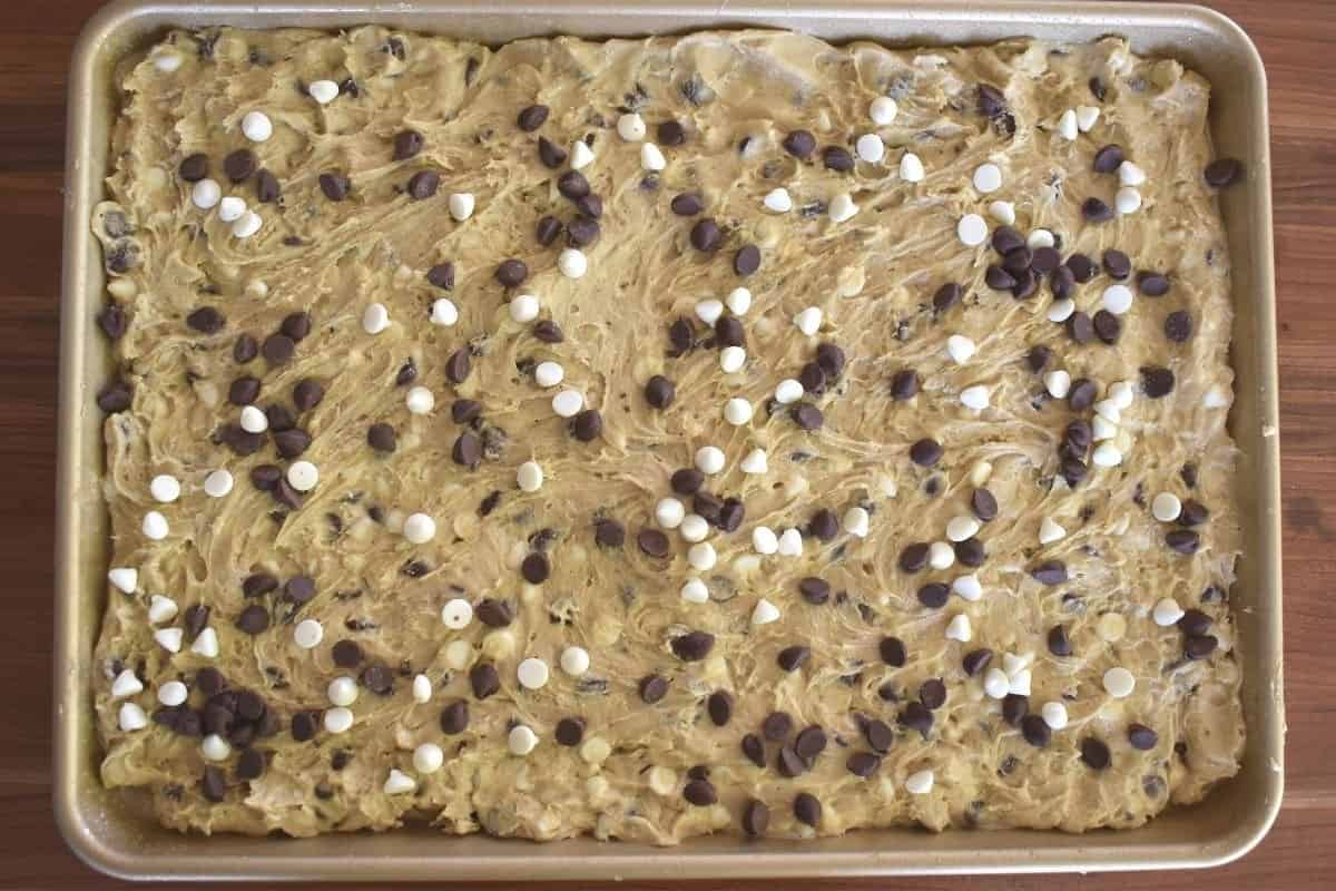 overhead photo of dough in the sheet pan with chocolate and white chocolate chips sprinkled over top. 