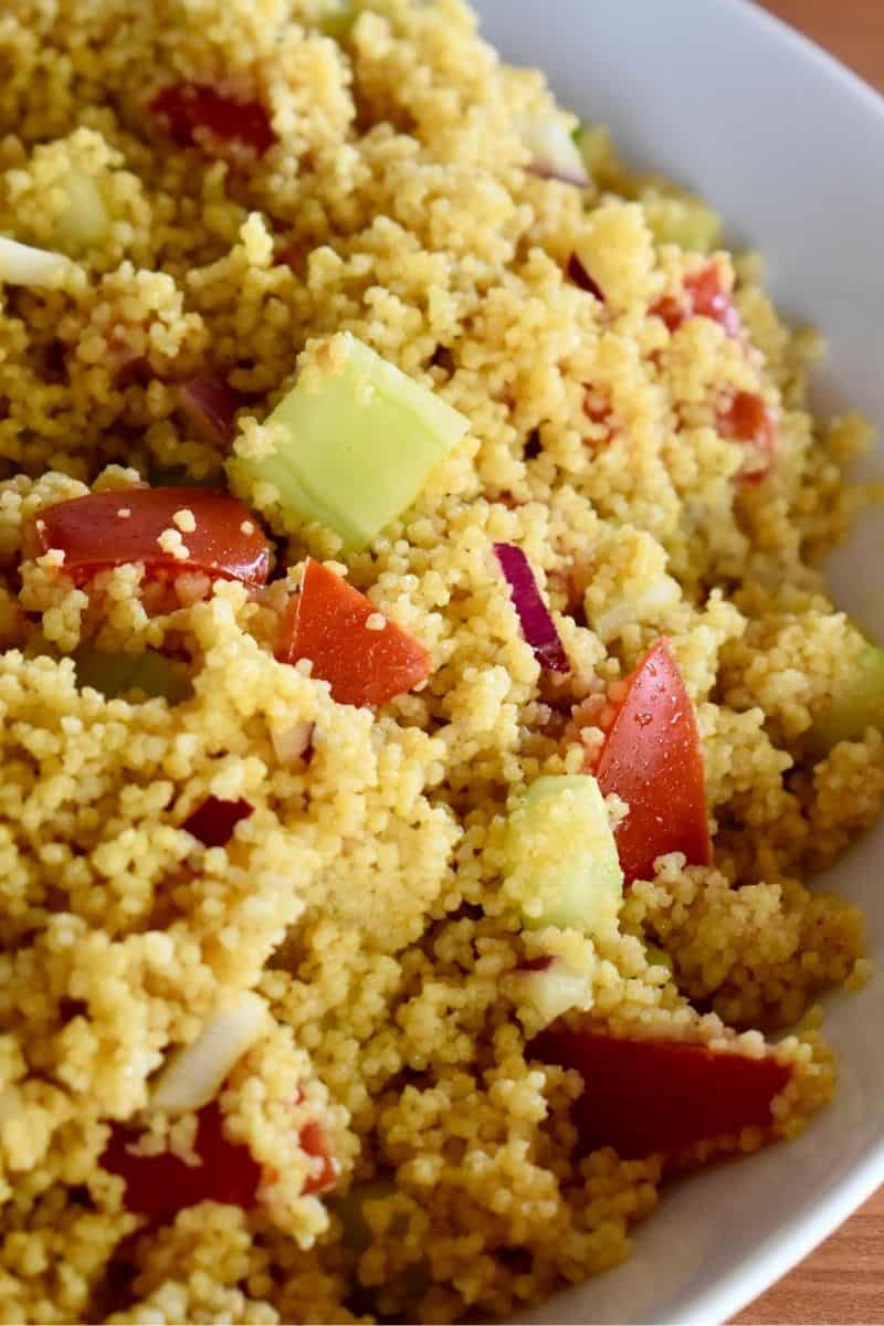 Curried Couscous in a white bowl with cucumbers, tomatoes, and red onion. 