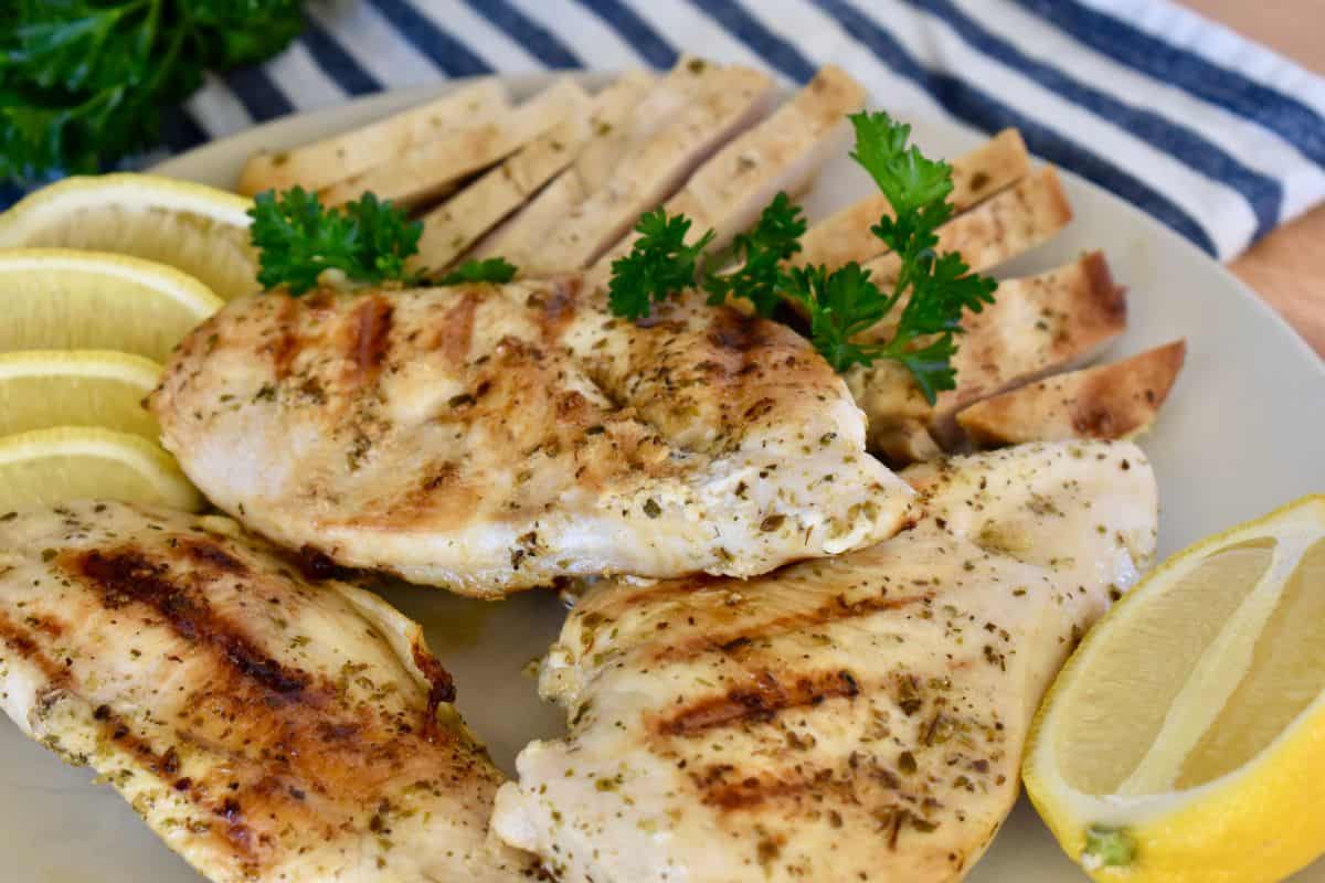 Greek Chicken on a white plate with parsley and lemons. 