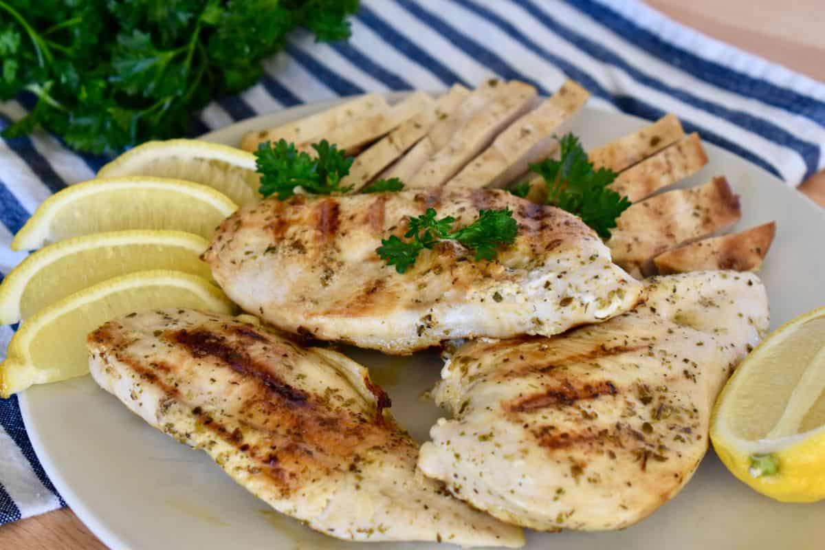 Greek chicken on a white plate with a blue and white striped napkin.