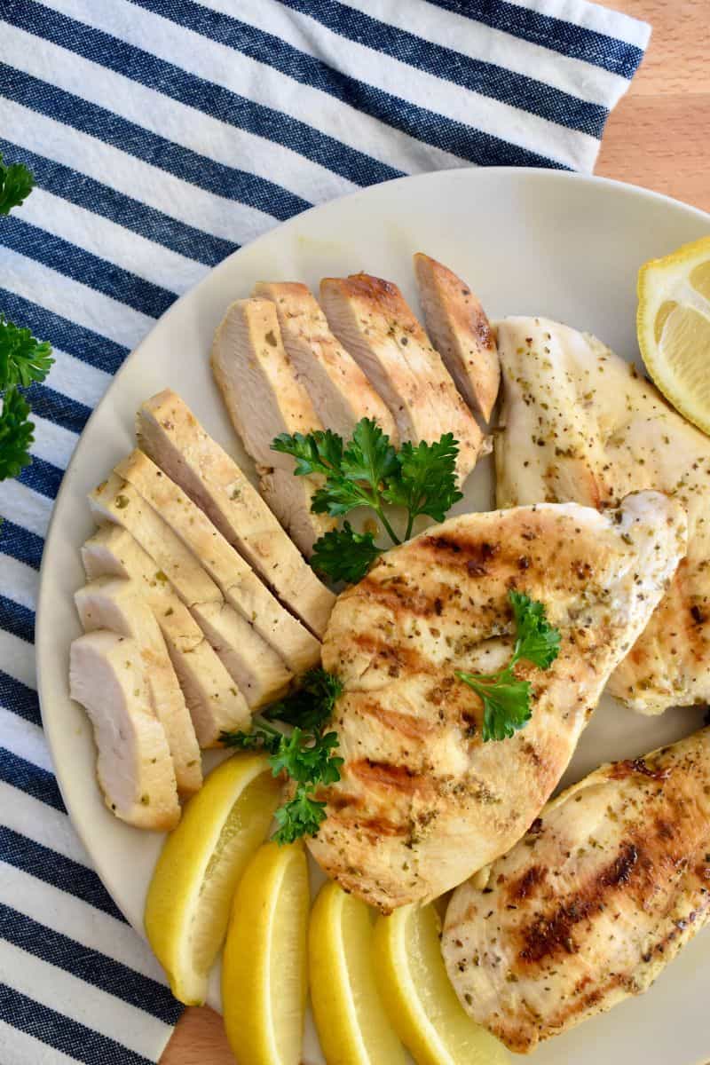 Greek Chicken Marinade recipe with chicken piled on a white bowl with lemon slices. 