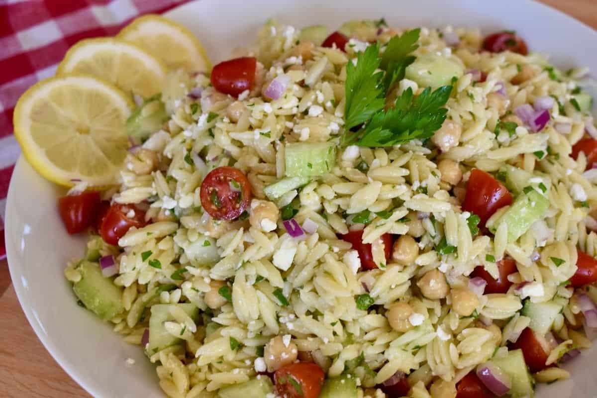 Lemon orzo salad in a white bowl with lemon slices next to it. 