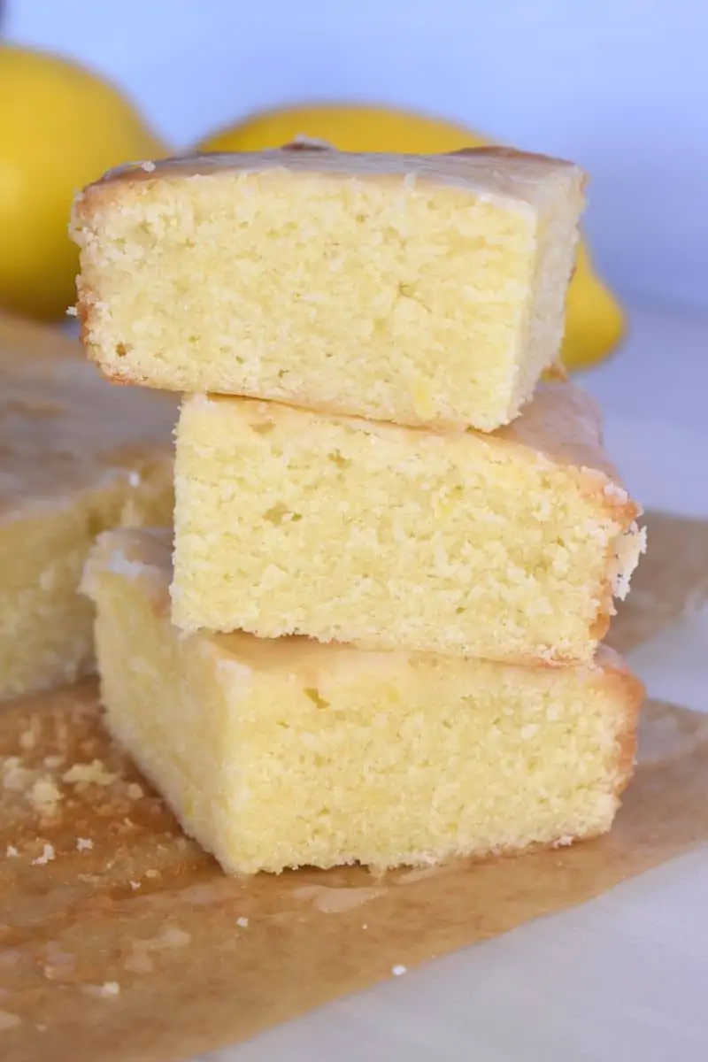 Lemon Blondies stacked on each other on a white counter with lemons in the background. 