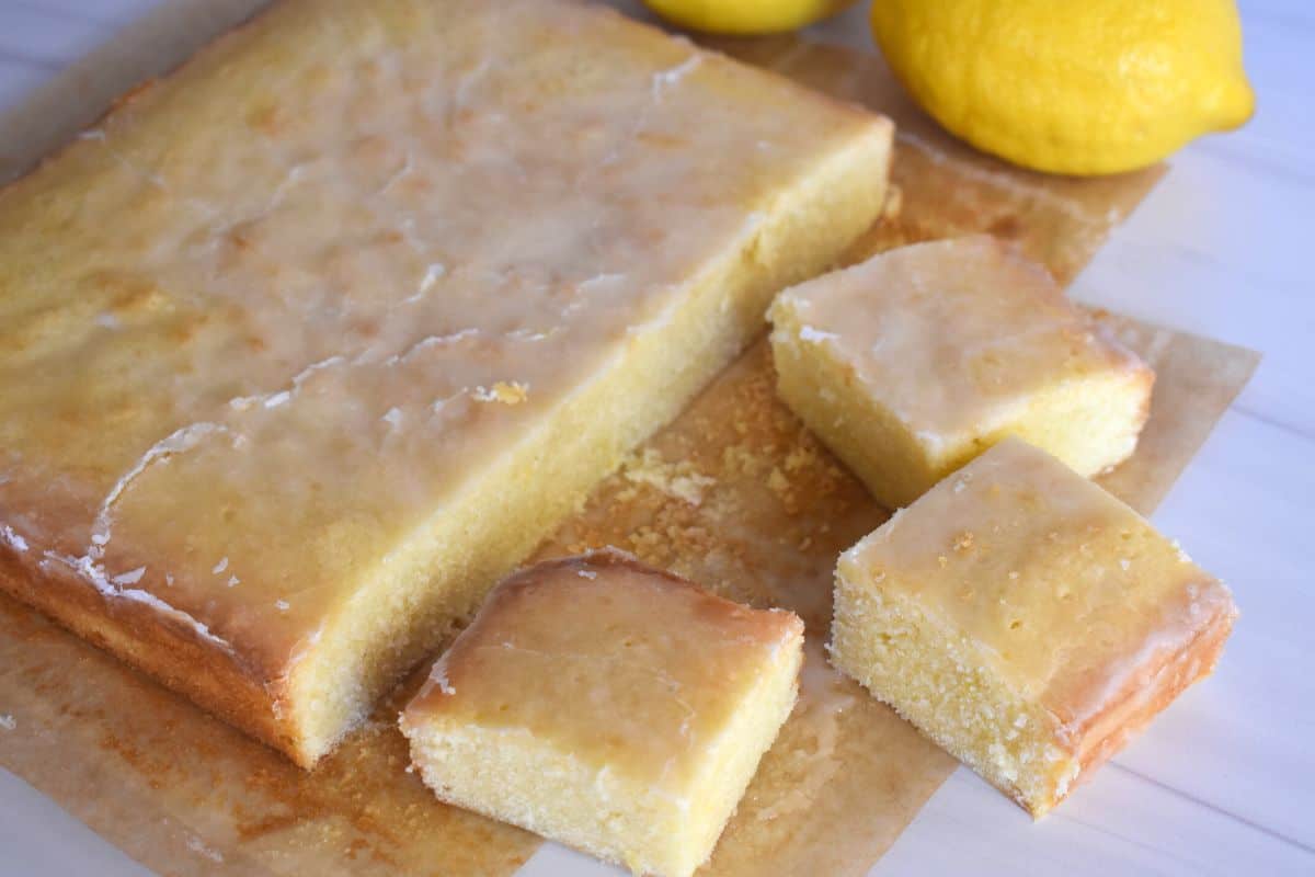 Lemon Blondies on a cutting board with three squares of the bars cut and lemons in the background. 