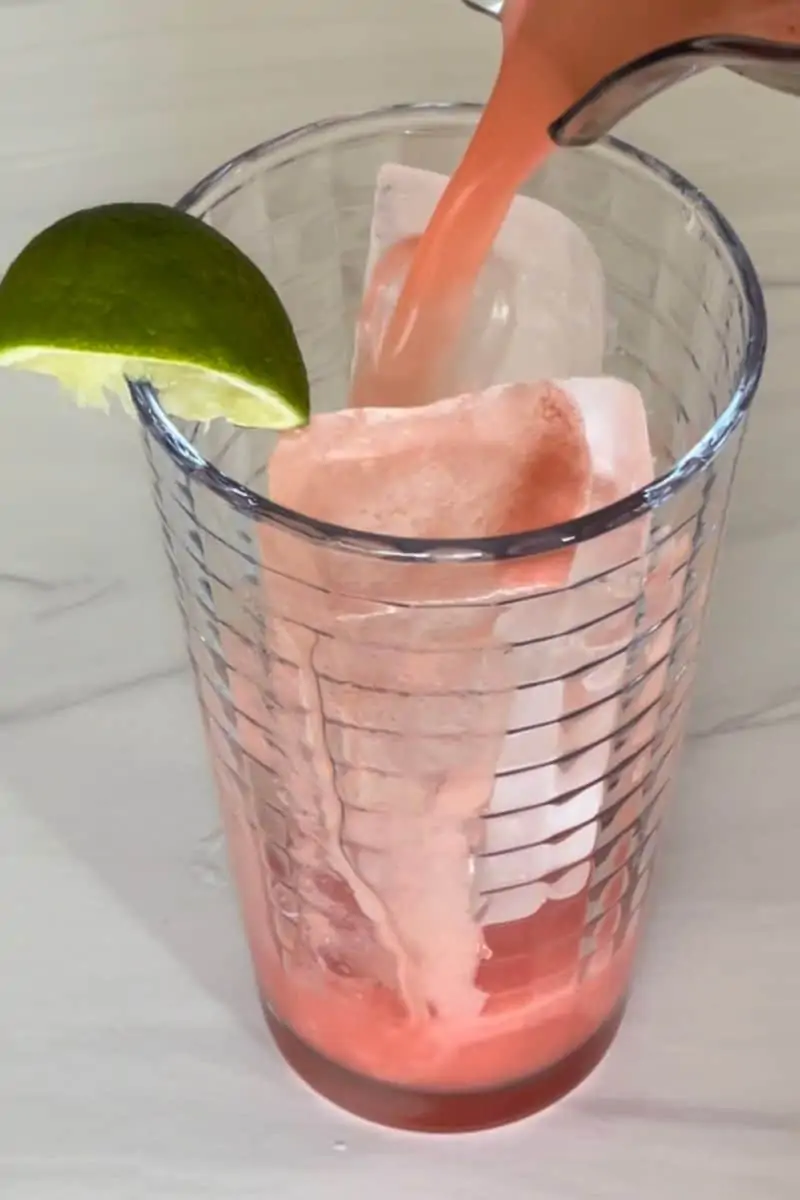 Watermelon Water being poured into a glass of ice with a lime wedge. 