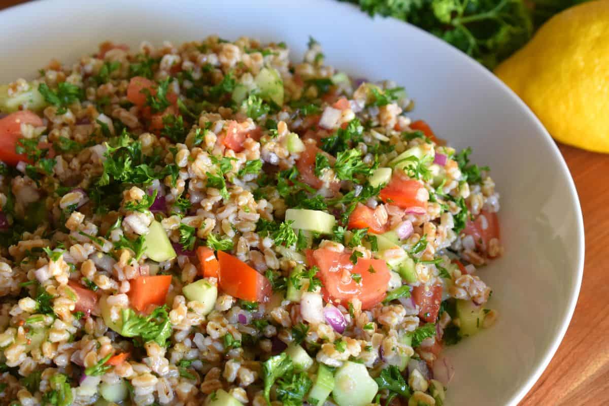 Farro Tabbouleh salad in a white bowl with lemon next to it. 