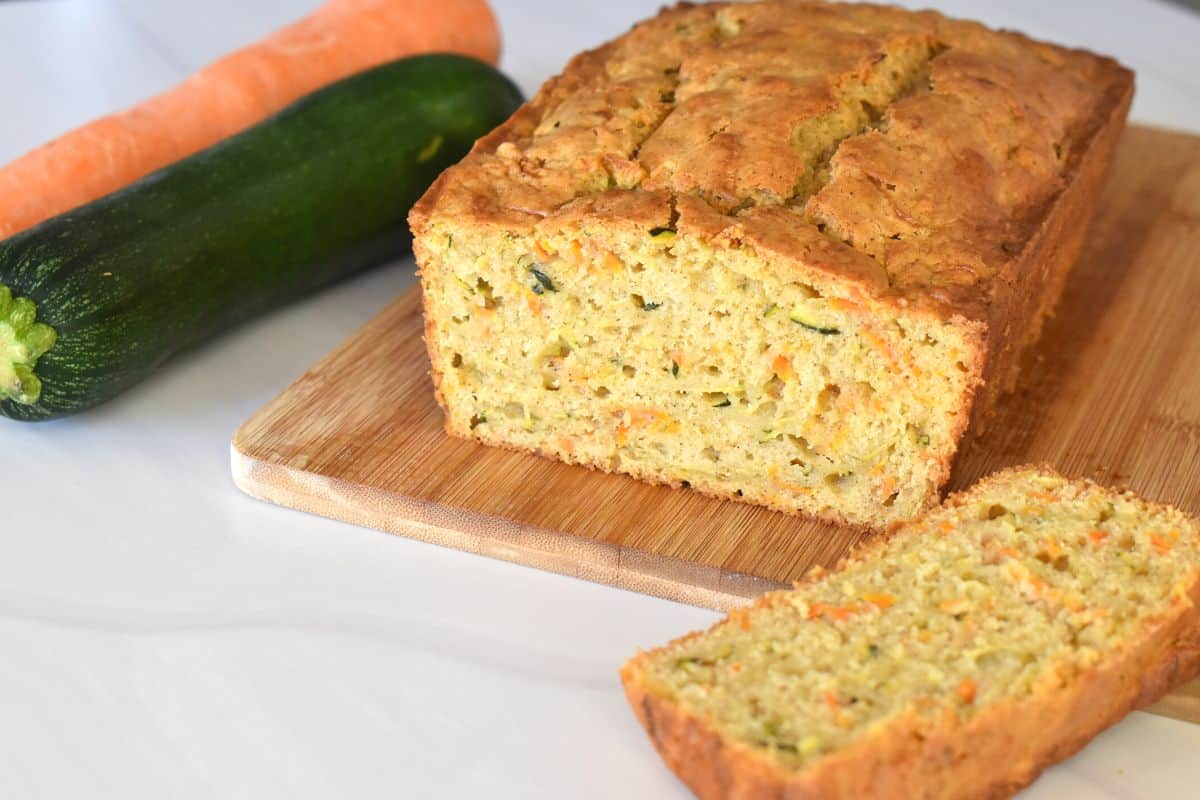 Zucchini Carrot Bread on a wood cutting board with a slice cut. 