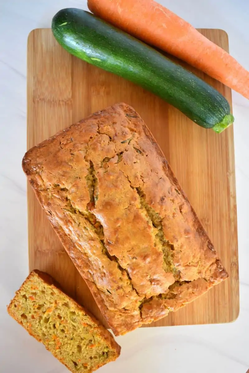 Overhead photo of Zucchini Carrot Bread on a cutting board with a zucchini and carrot next to it. 