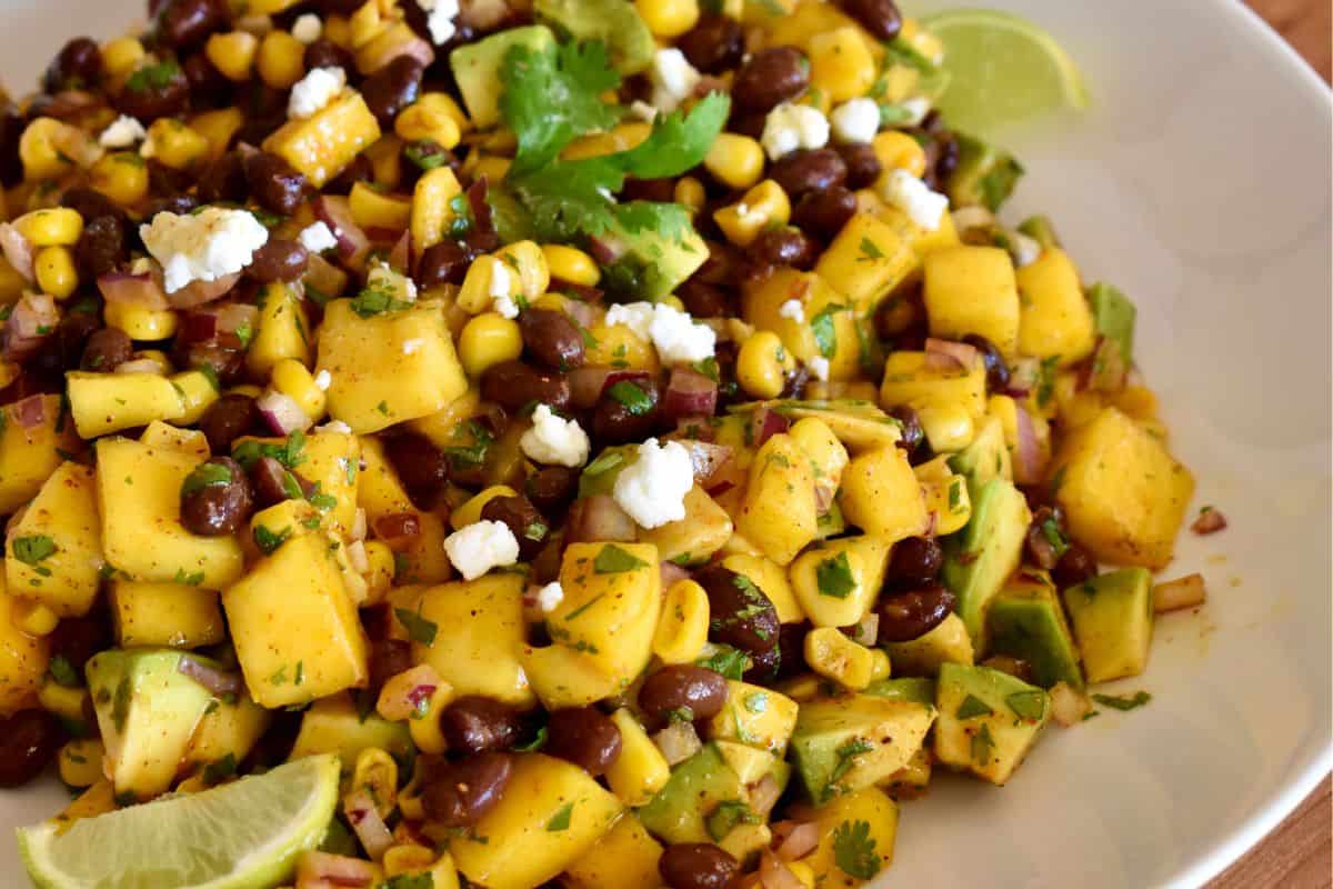 Mango Black Bean Salad in a white bowl with cilantro and lime garnish. 