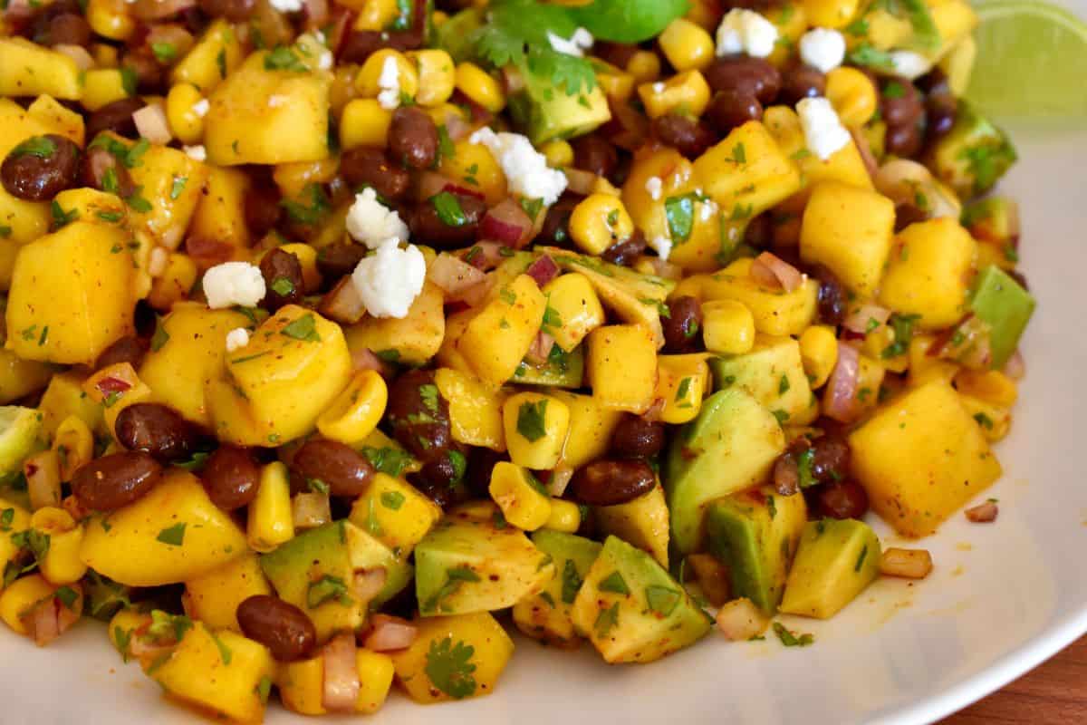 Mango Black Bean Salad in a white bowl with lime wedges and cilantro. 