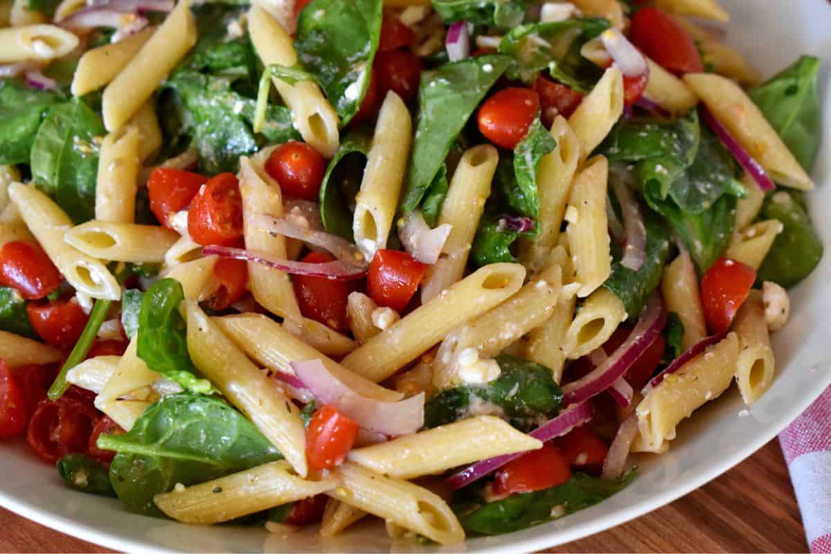 Spinach Pasta Salad with cherry tomatoes and red onions in a white serving bowl. 