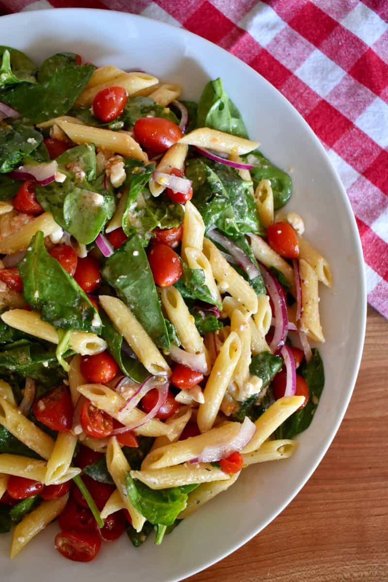 Spinach Pasta Salad in a white bowl with cherry tomatoes, red onion, and feta cheese. 