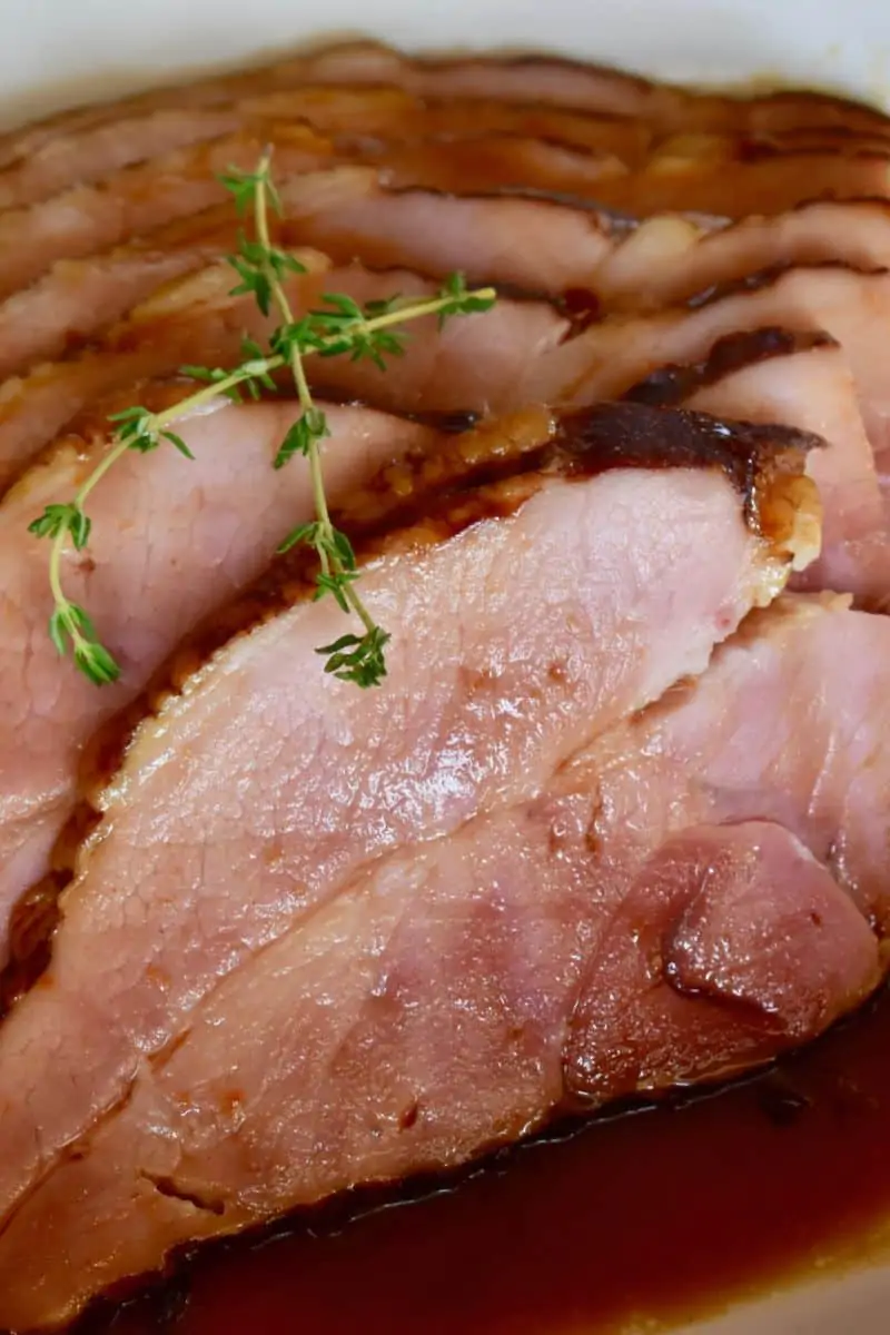 sliced slow cooker ham on a white plate with a sprig of thyme on top. 